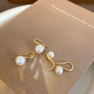 Elegant white shell pearl earrings with gold hooks on a warm minimalist background