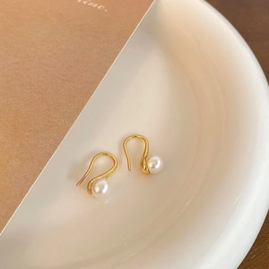 Macro detail of high-heeled S-shaped gold-plated pearl drop earrings on white ceramic tray