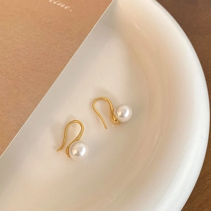 Close-up of elegant gold-plated high heel pearl drop earrings on white ceramic dish
