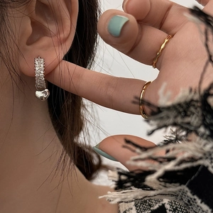 Close-up of heart charm earrings with zircon inlay and silver hoop on model's ear