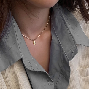 Gros plan d'un collier de perles dorées minimaliste avec pendentif ovale gravé