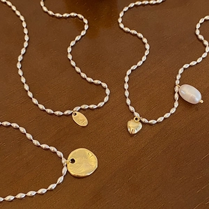 Détail de colliers en perles argentées avec pendentifs cœur doré, lettre A et perle