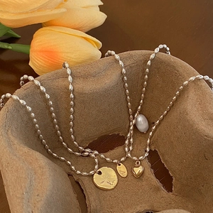 Détail de la chaîne perlée argentée avec pendentif cœur doré, disque solaire et perle