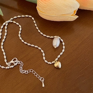 Détail du pendentif perle baroque et cœur doré sur un collier à chaîne perlée argentée