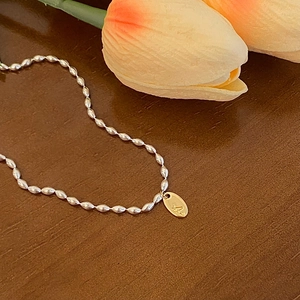 Détail d'un collier à billes argentées avec pendentif ovale doré gravé de la lettre A