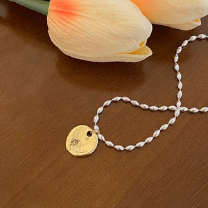 Détail d'une chaîne à billes argentée et d'un pendentif doré martelé sur bois rustique