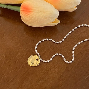 Détail d'un collier bicolore vintage français avec pendentif pièce d'or sur fond bois