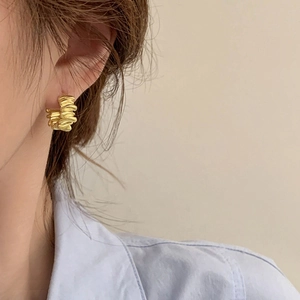 Gros plan de boucles d'oreilles dorées avec texture froissée et vagues vintage