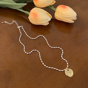 Détail du pendentif soleil doré et chaîne perlée argentée sur fond en bois