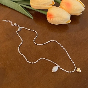 Détail du collier à billes argentées avec pendentif cœur doré et perle blanche ovale