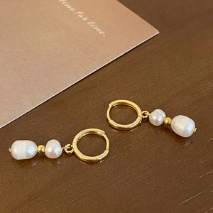 Detailed macro view of baroque pearl earrings with golden hoops on a vintage desk