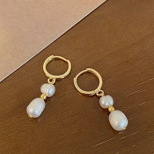 Detailed view of gold hoop earrings featuring irregular baroque pearls on wooden surface