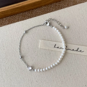 Détail du bracelet en perles et chaîne argentée avec fermoir sur tissu beige
