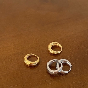 Macro detail of irregular geometric hoop earrings in gold and silver finish with faceted edges