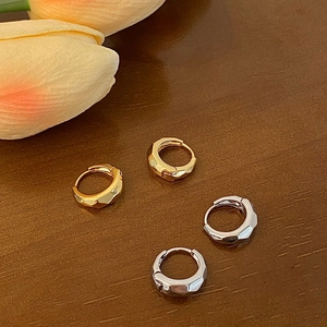 Detailed view of geometric gold and silver hoop earrings on a textured wooden background