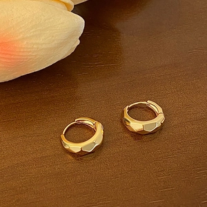 Macro shot of faceted gold hoop earrings with geometric edges on a wooden surface