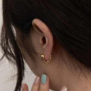 Macro shot of polished gold hollow heart-shaped earrings on model for detail view