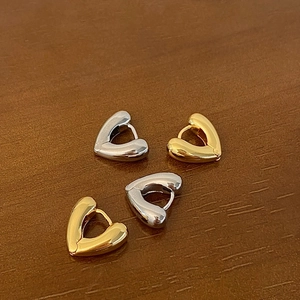 Close-up detail of gold and silver hollow heart-shaped hoop earrings on wood surface