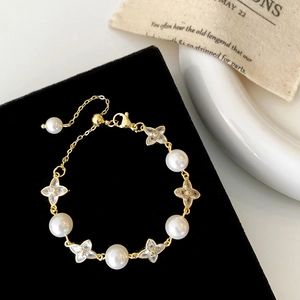 Detail of gold pearl bracelet with clover charms on black velvet display stand