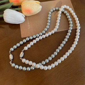 Dettaglio di collane di perle crema e grigio argento con chiusure ovali su legno