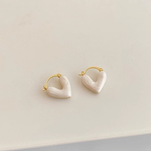 Macro shot of gold-plated heart earrings featuring pearlescent white enamel drops