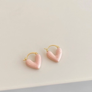 Close-up of heart-shaped drop earrings with pink pearlescent finish and gold hoops