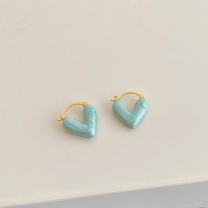 Macro shot of light blue heart-shaped enamel earrings with gold-plated metal hoops