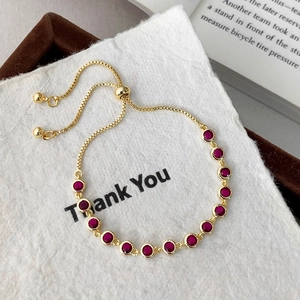 Detail of adjustable gold box chain bracelet with sparkling red round-cut gemstones