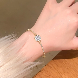 Detail of square-cut zircon bracelet in gold with sparkling halo on woman's wrist