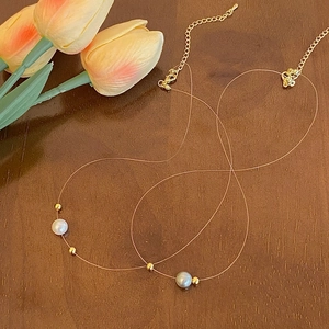Detail of invisible fishing line necklace with white and grey pearls on wood surface
