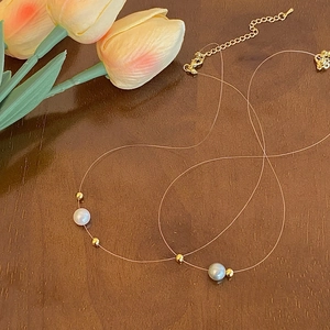 Minimalist pearl necklace on fish line with gold beads and extension chain on wood