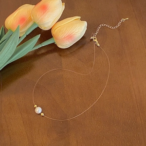 Detail of elegant white pearl pendant on thin invisible line with gold plating
