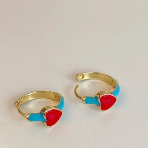 Close-up of gold-plated red enamel heart earrings on a minimalist white background