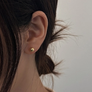 Close-up of a minimalist golden spherical stud earring worn on the earlobe with high shine