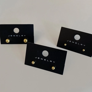 Detailed view of three pairs of round gold stud earrings on black jewelry card display