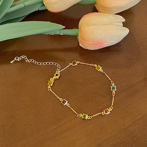 Bracelet doré serti de pierres précieuses carrées colorées sur fond en bois rustique