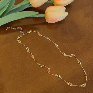 Détail d'un collier doré avec gemmes colorées carrées sur fond bois rustique