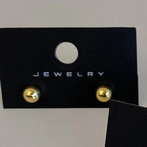 Close-up of minimalist golden spherical stud earrings with polished mirror finish on black card