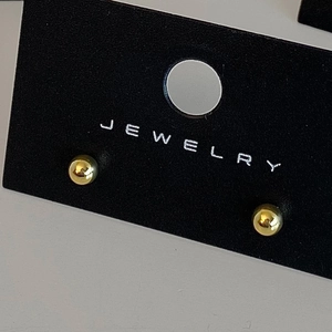 Detailed view of minimalist gold sphere stud earrings on a professional black jewelry card