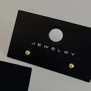 Detailed view of glossy gold sphere stud earrings displayed on a black jewelry card