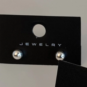 Macro shot of minimalist silver ball stud earrings on a black jewelry display card