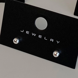 Macro shot of polished silver ball stud earrings displayed on a black jewelry card