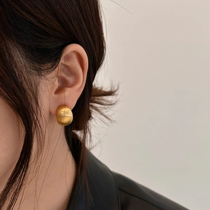 Close-up of minimalist matte gold bean stud earrings with a brushed metal finish texture