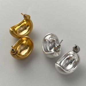 Macro detail of gold and silver bean-shaped stud earrings with matte metal texture