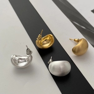 Macro detail of brushed matte bean-shaped stud earrings in gold and silver finish