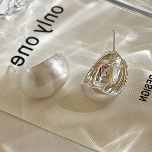 Macro detail of silver bean stud earrings featuring a matte brushed metal finish