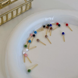 Close-up of minimalist colorful bean stud earrings displayed on a white ceramic plate