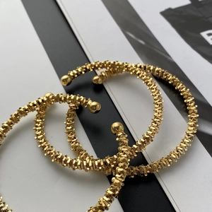 Close-up of three golden open bracelets with textured serrated surface and sphere ends