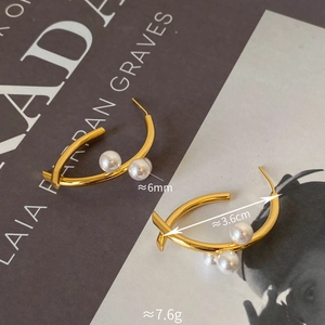 Détail de boucles d'oreilles dorées croisées avec perles blanches sur magazine