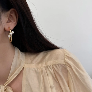 Gros plan de boucles d'oreilles croisées dorées avec trois perles sur un mannequin